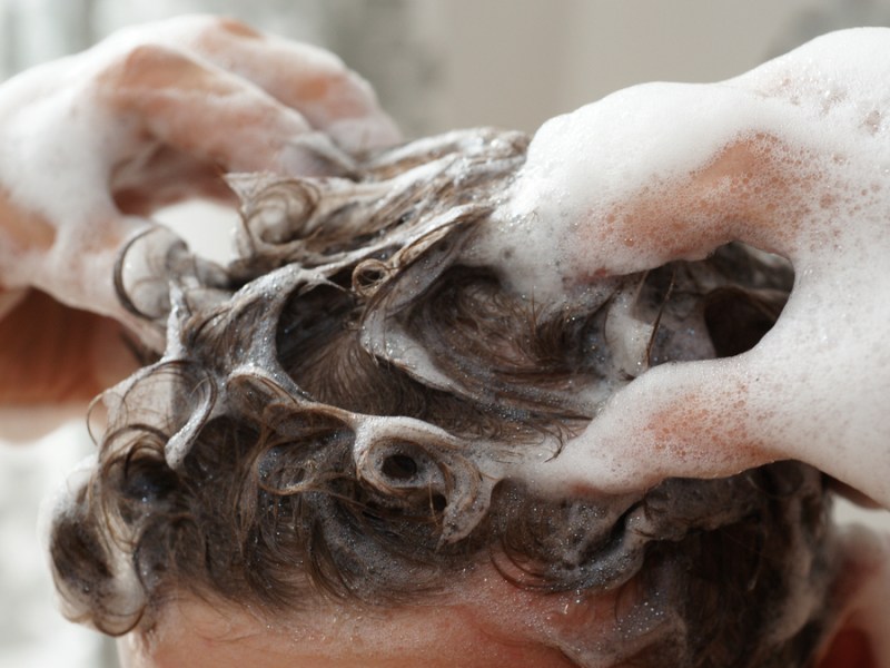 Jemand massiert seine Haare mit Shampoo ein.