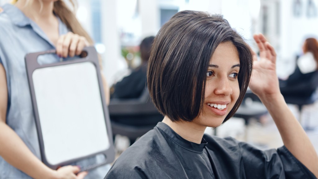 Eine Frau mit Bob-Frisur betrachtet ihr Haar beim Friseur.