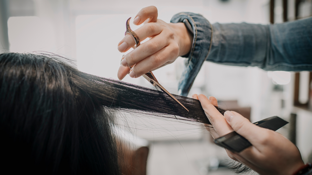 Eine Friseuse schneidet eine Strähne schwarzen Haares einer Kundin.