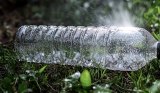 Ein Bild zeigt, wie man den Rasen mit einer Plastikflasche bewässern kann.