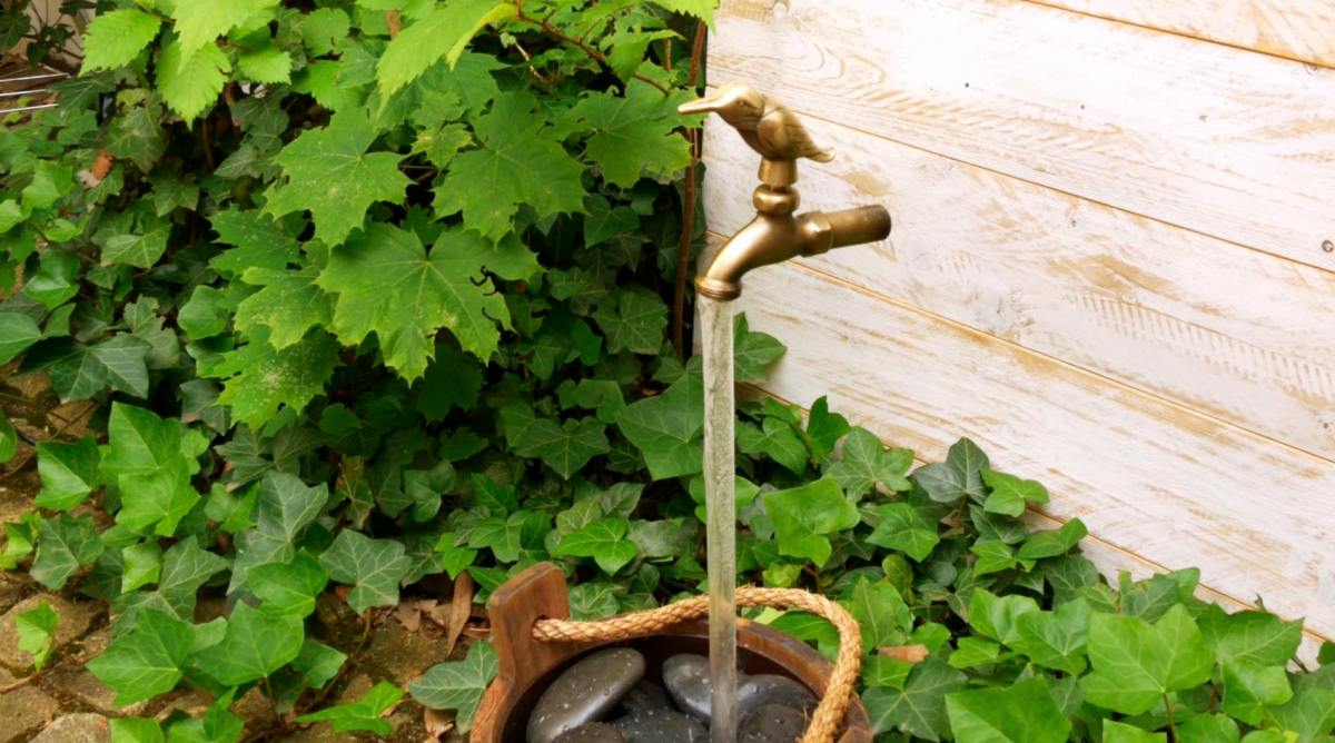 Ein schwebender Wasserhahn als Gartendeko an einer Hauswand.
