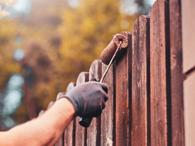 Eine Frau streicht einen Gartenzaun.