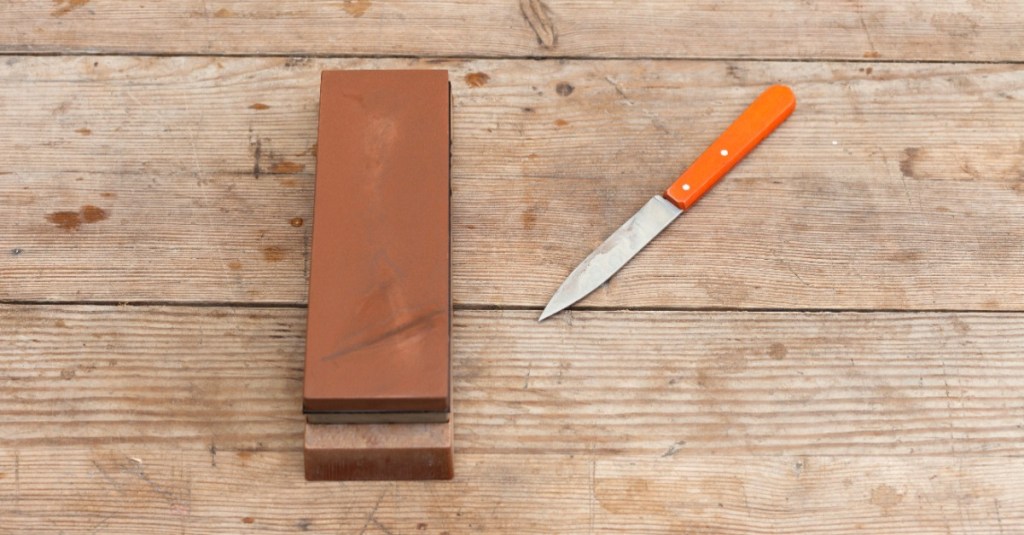 ein Messer mit einem orangen Griff liegt neben einem Wetzstein