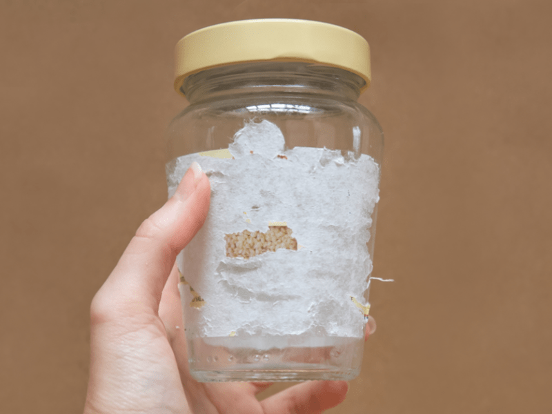 Jemand hält ein Glas in der Hand, bei welchem das Etikett nicht vollständig entfernt werden konnte. Mithilfe des Kriechöls WD-40 kannst du den Aufkleber lösen und restlos entfernen.