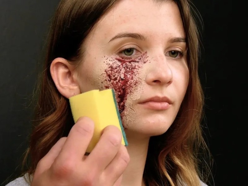 Eine junge Frau trägt mit einem Putzschwamm Halloween-Make-up auf.