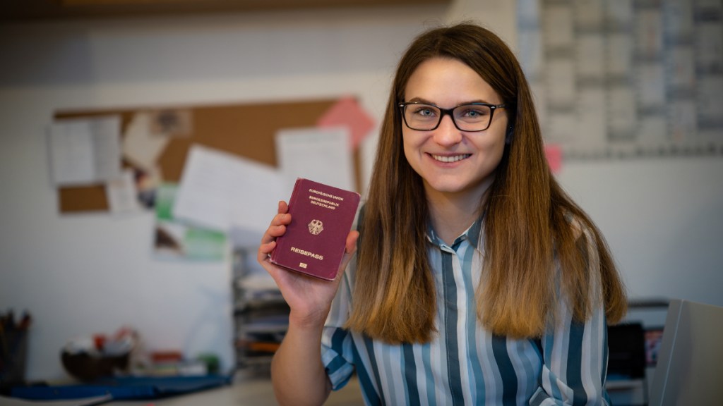 Eine junge Frau hält stolz ihren Reisepass hoch.