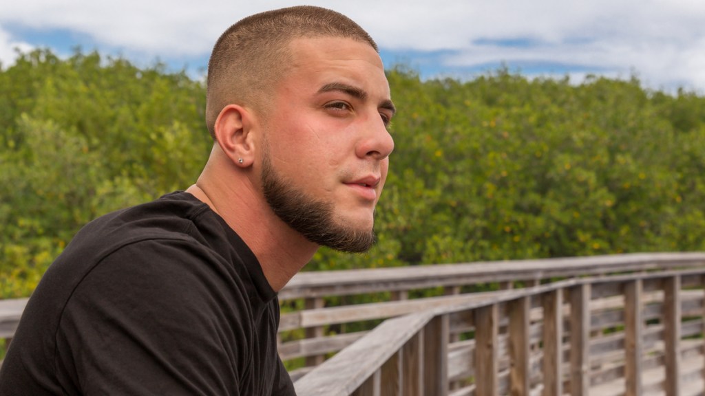 Ein Mann mit Buzzcut steht einer hölzernen Brücke.