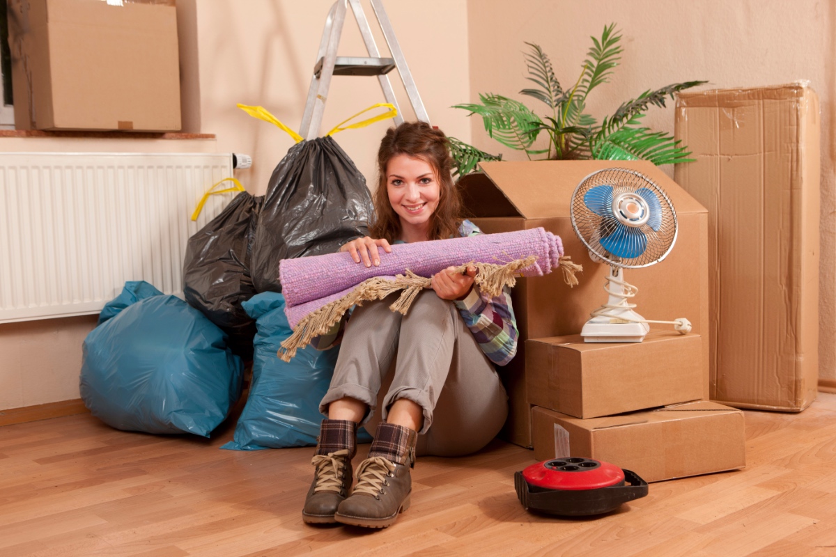 Eine Frau sitzt in ihrer ausgeräumten Wohnung zwischen Kartons und Müllsäcken.