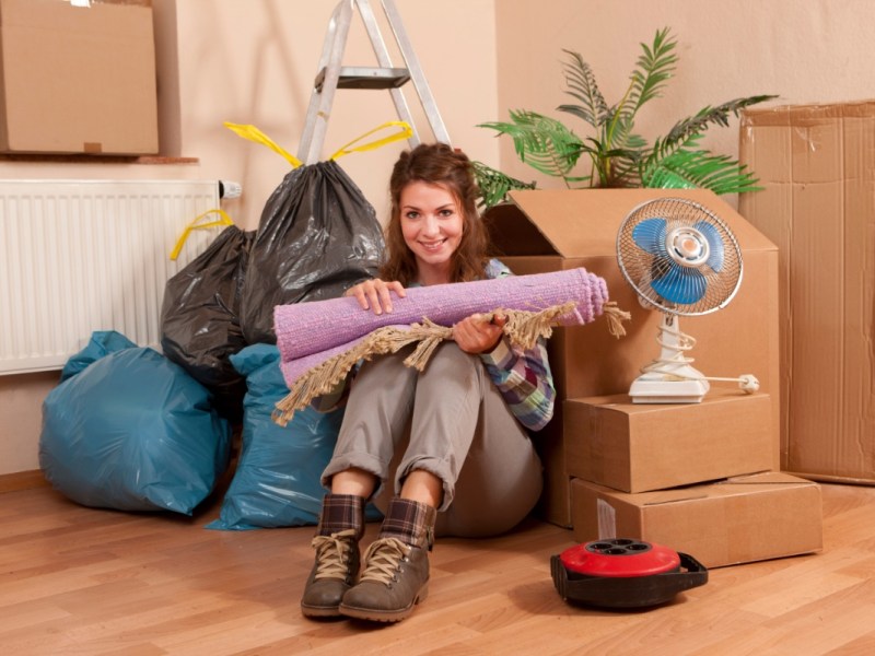 Eine Frau sitzt in ihrer ausgeräumten Wohnung zwischen Kartons und Müllsäcken.