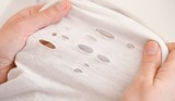 Eine Frau zieht weißen Stoff auseinander und zeigt kleine Löcher in weißer Kleidung.