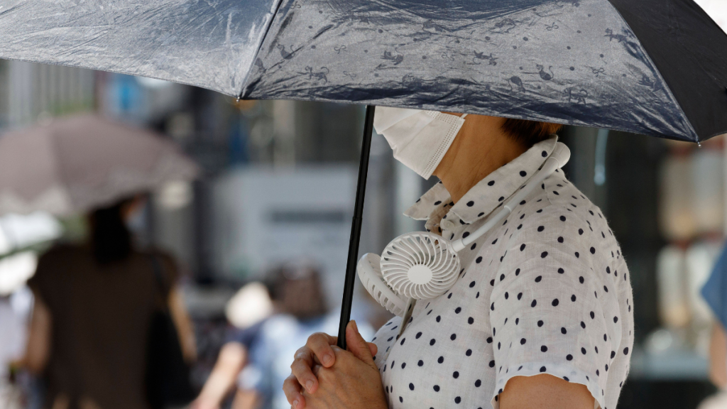 Eine Person mit Regenschirm und einem weißen Hals-Ventilator.