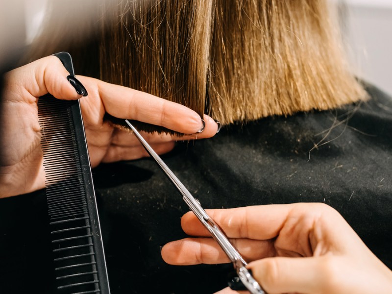 Einer Frau werden die Haare mit Kamm und Schere geschnitten.