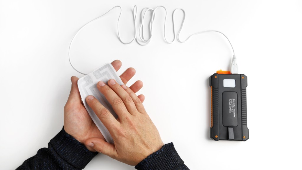 Ein Mann hält seine beiden Hände an einen Handwärmer, der mit einem USB-Kabel geladen wird.
