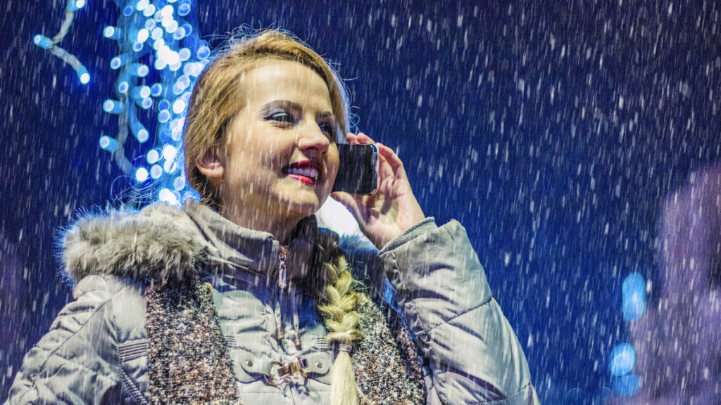 Eine Frau telefoniert während eines Schneeschauers mit ihrem Smartphone.