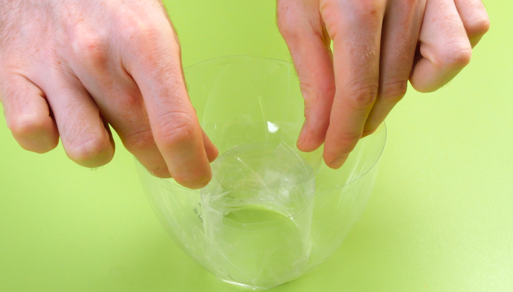 Klebeband wird auf ein Stück aus einer Plastikflasche geklebt.