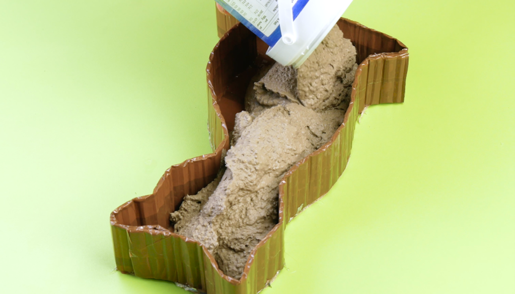 Bastelbeton wird in eine Katzenform aus Pappe gegossen.