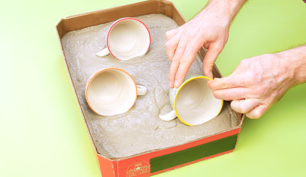 Tassen werden in einen Karton mit Bastelbeton gedrückt.