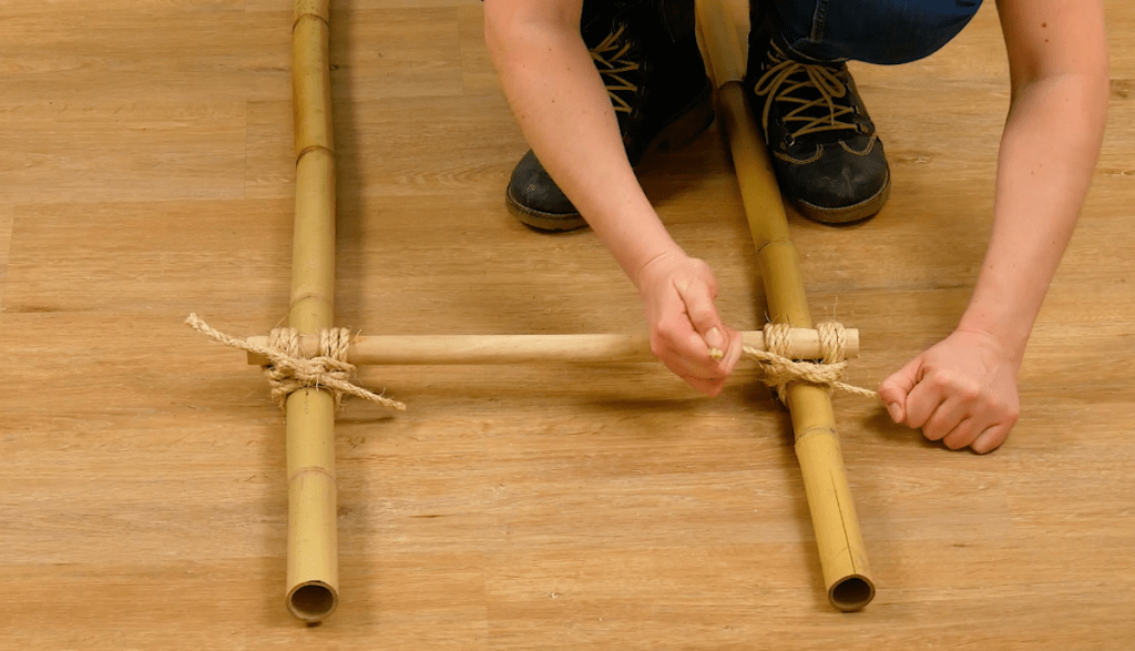 Bambusstangen und Holzstangen werden mit Juteseil zu einer Art Leiter zusammen geknotet.