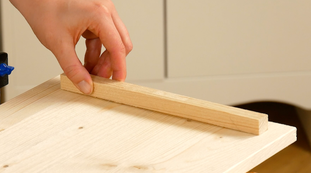 Eine Holzleiste wird auf ein Brett geklebt.