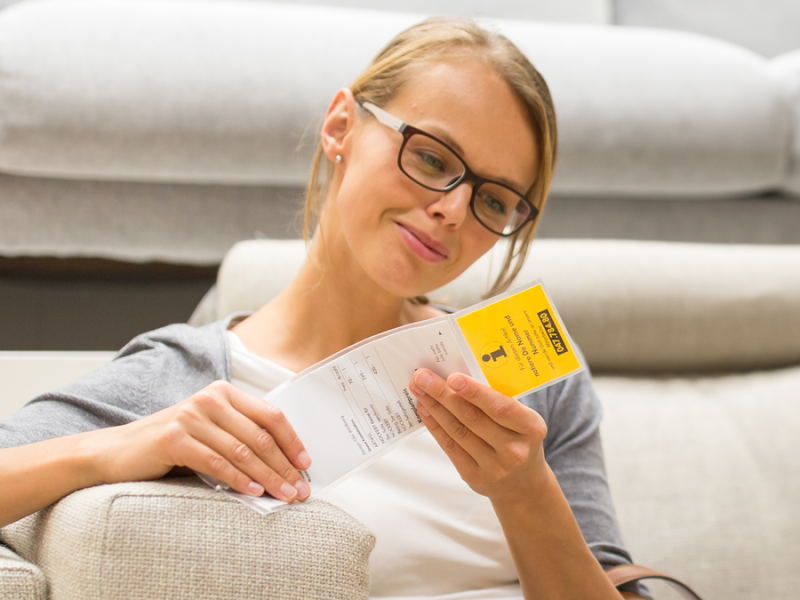 Eine Frau sitzt auf einer IKEA-Couch und schaut sich das Preisschild an.