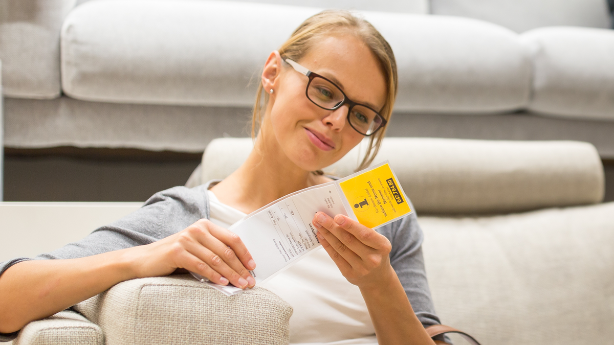 Eine Frau sitzt auf einer IKEA-Couch und schaut sich das Preisschild an.