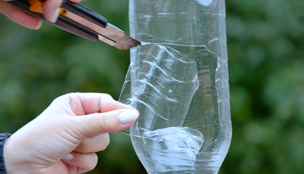 Ein Rechteck wird mit einem Cuttermesser aus einer leeren Plastikflasche geschnitten