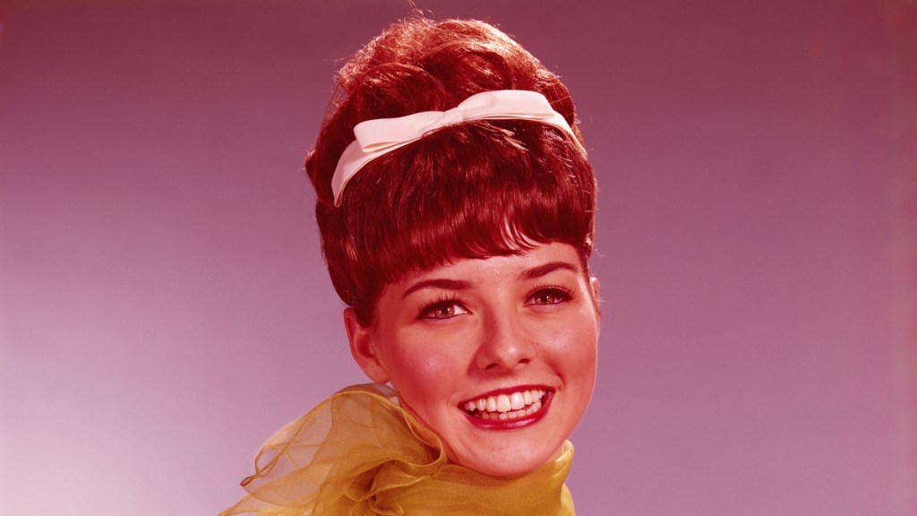 Eine Frau mit einer Beehive-Frisur und einer weißen Schleife im Haar.
