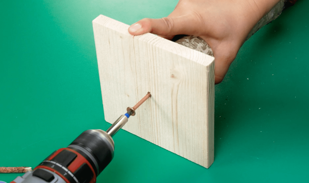 Eine kleine Holzplatte wird an einen dicken Ast geschraubt