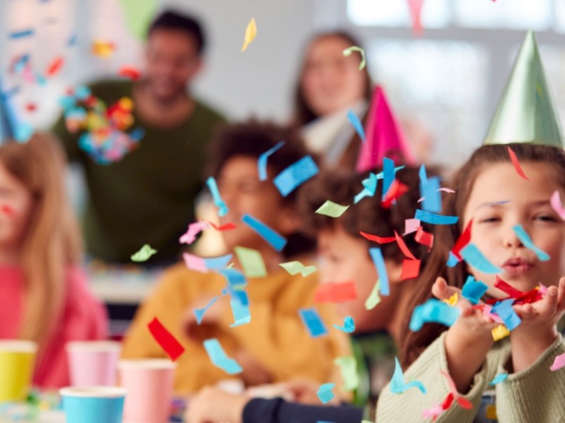 Kind pustet Konfetti am Geburtstag durch die Luft