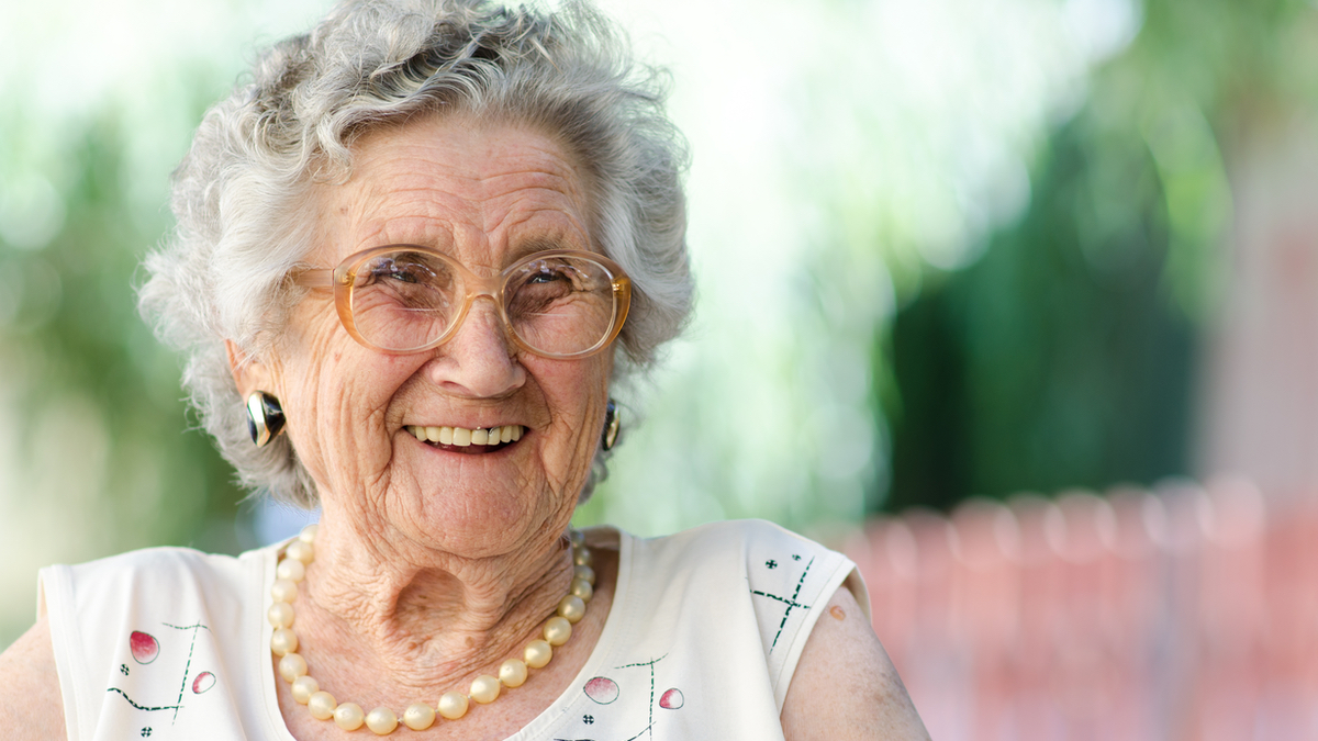 Eine ältere Frau mit grauen Haaren lächelt in die Kamera.