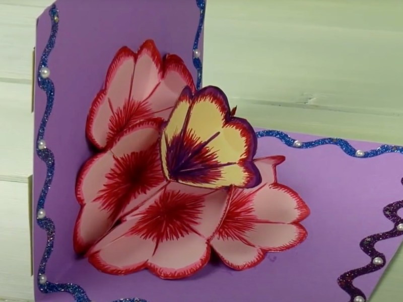 Eine aufgeklappte selbst gebastelte Geburtstagskarte mit einer Blüte aus Papier in der Mitte.