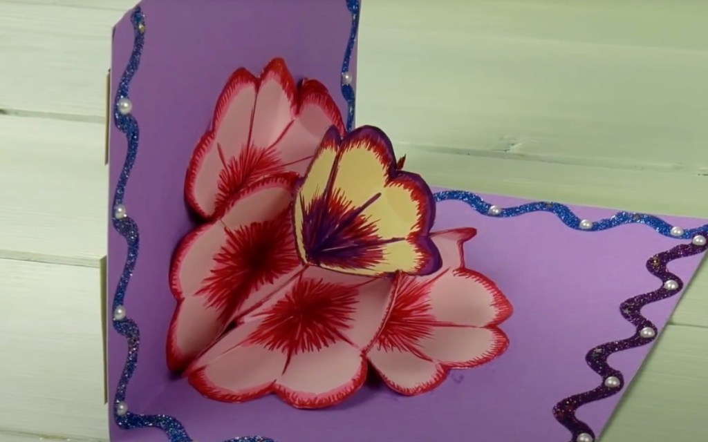 Eine aufgeklappte selbst gebastelte Geburtstagskarte mit einer Blüte aus Papier in der Mitte.