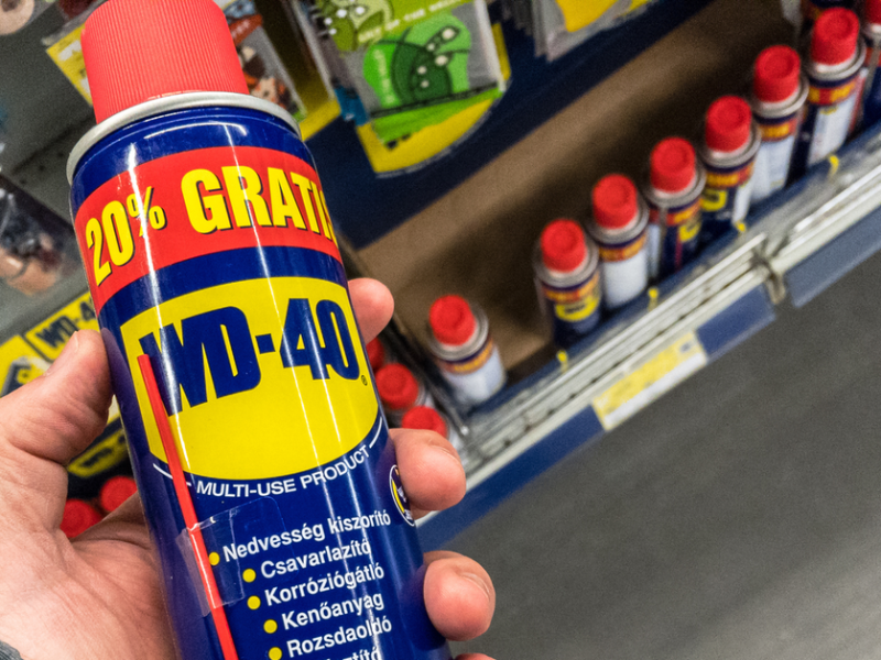 Jemand hält WD-40 in die Kamera. Im Hintergrund sieht man ein Regal mit weiteren Dosen des Kriechöls.