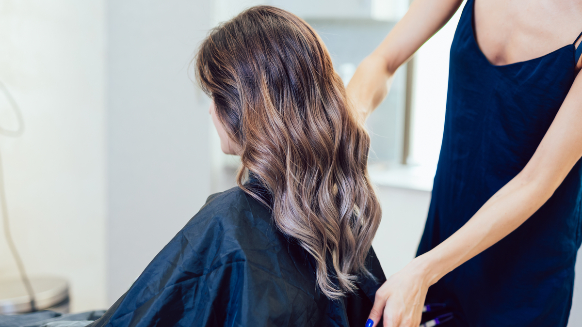 Eine Frau mit langen braunen Haaren sitzt beim Friseur.