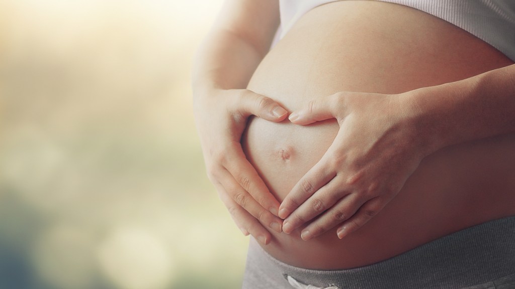 Eine schwangere Frau umfasst ihren Babybauch.