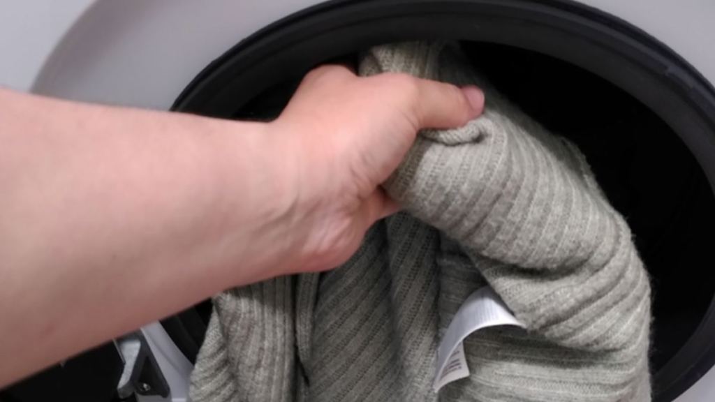 Ein Wollpullover wird in eine Waschmaschine gesteckt.
