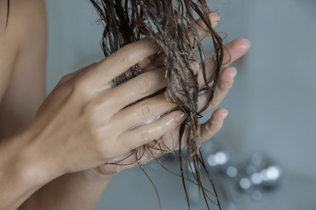 Eine Frau knetet Conditioner in ihre Haarspitzen ein.
