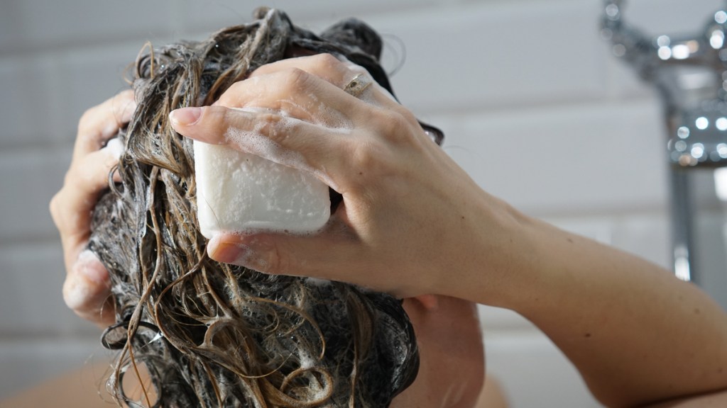 Eine Frau schäumt ihre Haare mit einem Stück Seife ein.