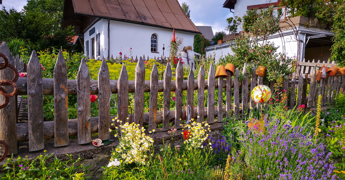 Ein bunt bepflanzter Garten mit einem Holzzaun und einem Haus im Hintergrund