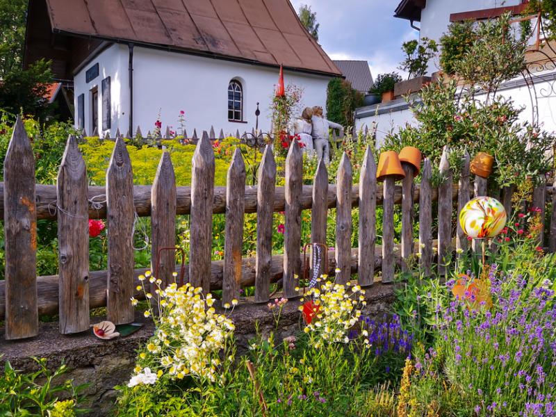 Ein bunt bepflanzter Garten mit einem Holzzaun und einem Haus im Hintergrund
