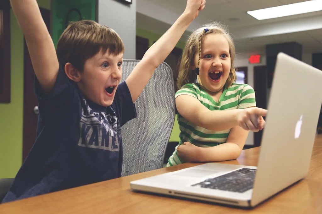 Zwei Kinder sitzen vor einem MacBook und freuen sich.