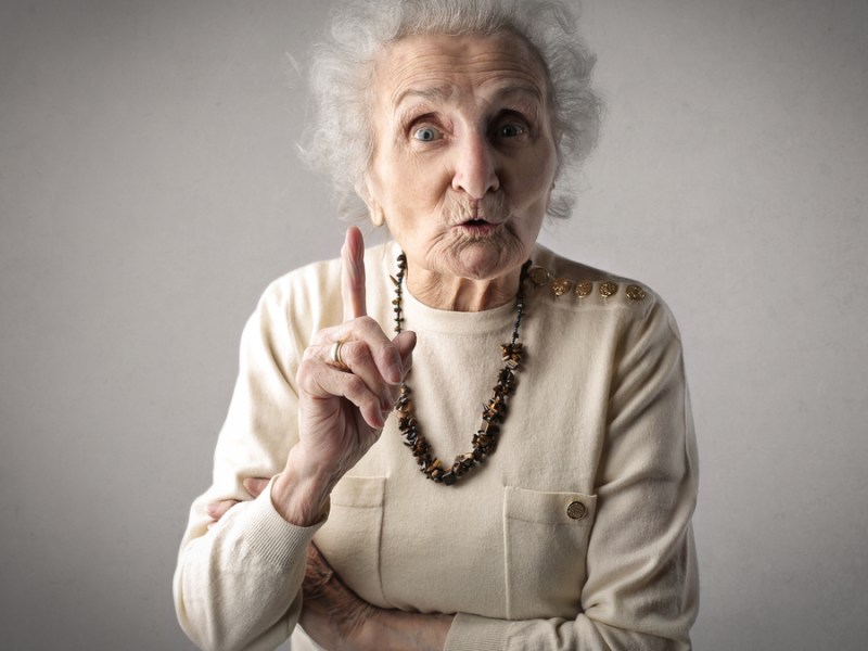Eine Seniorin hebt ermahnend den rechten Zeigefinger.