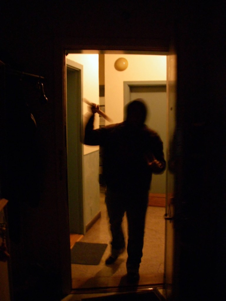 Ein Einbrecher im Flur an der offenen Wohnungstür.