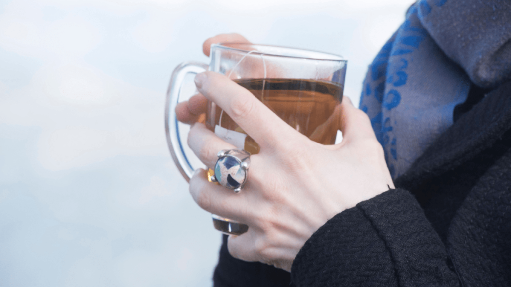 Eine Frau hält ein Teeglas mit braunem Tee darin fest.