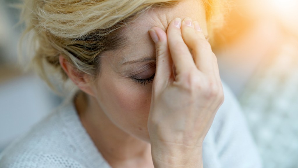 Eine blonde Frau greift sich mit einer Hand an den Kopf.