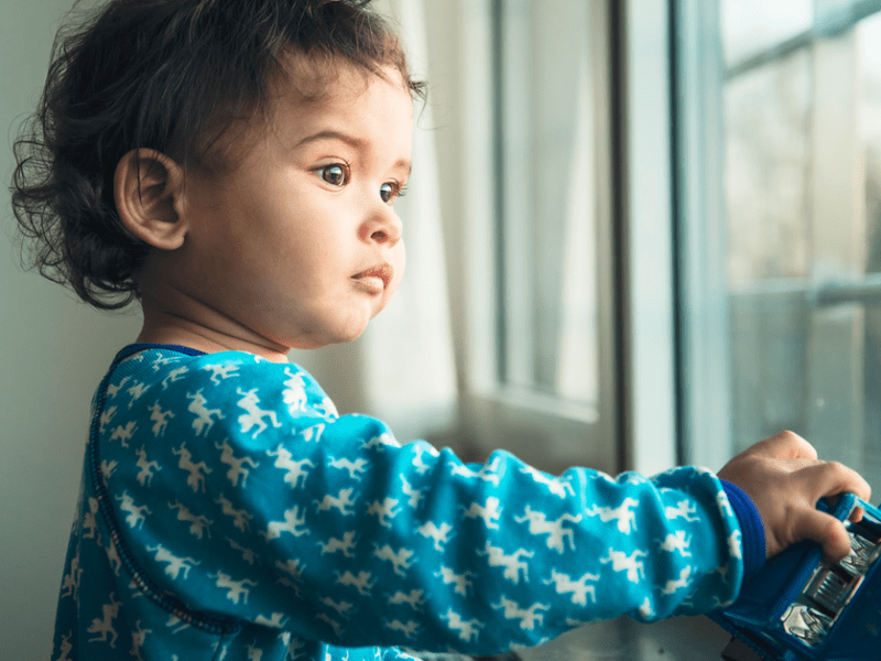 Ein Kind hält ein Spielzeugauto in der Hand und schaut aus einem Fenster