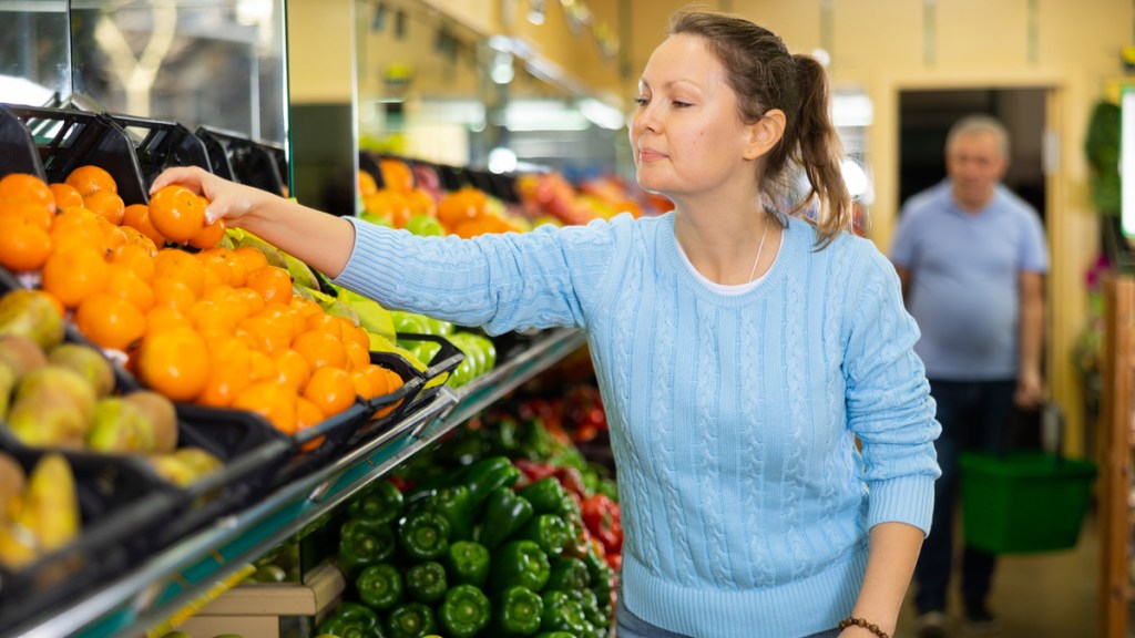 Eine Frau greift im Supermarkt nach aufgelegten Mandarinen.