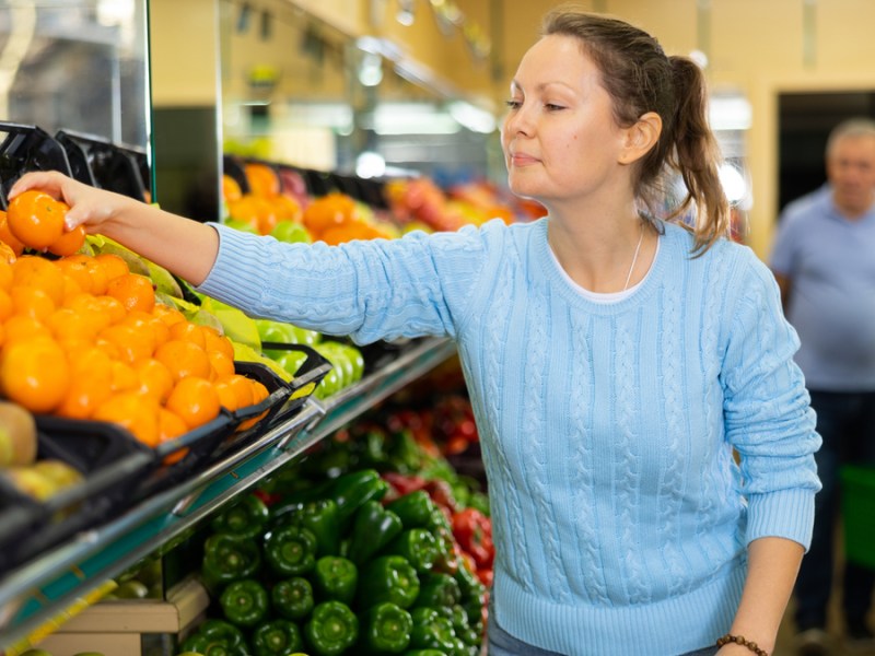 Eine Frau greift im Supermarkt nach aufgelegten Mandarinen.