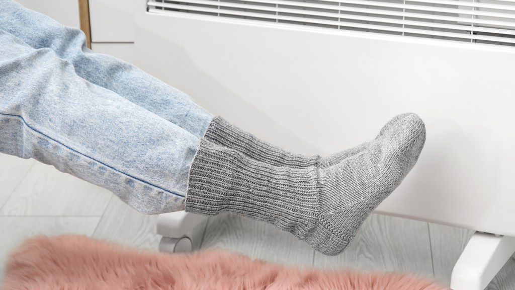 Eine Frau in dicken, grauen Socken vor einem Heizkörper.