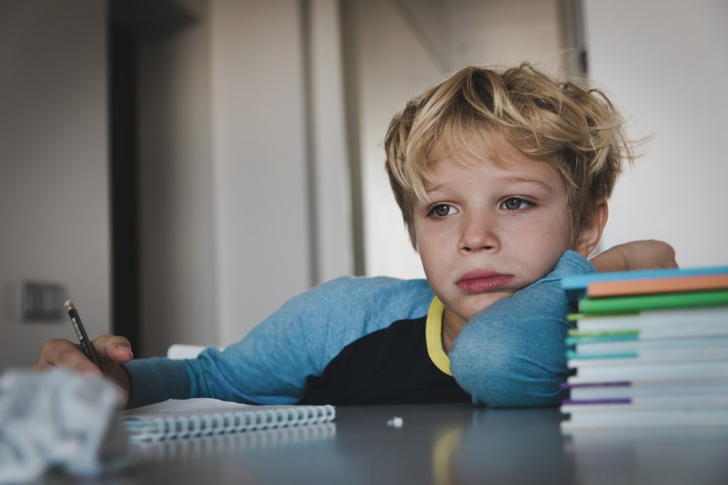 Ein Junge sitzt an einem Schreibtisch und schaut traurig